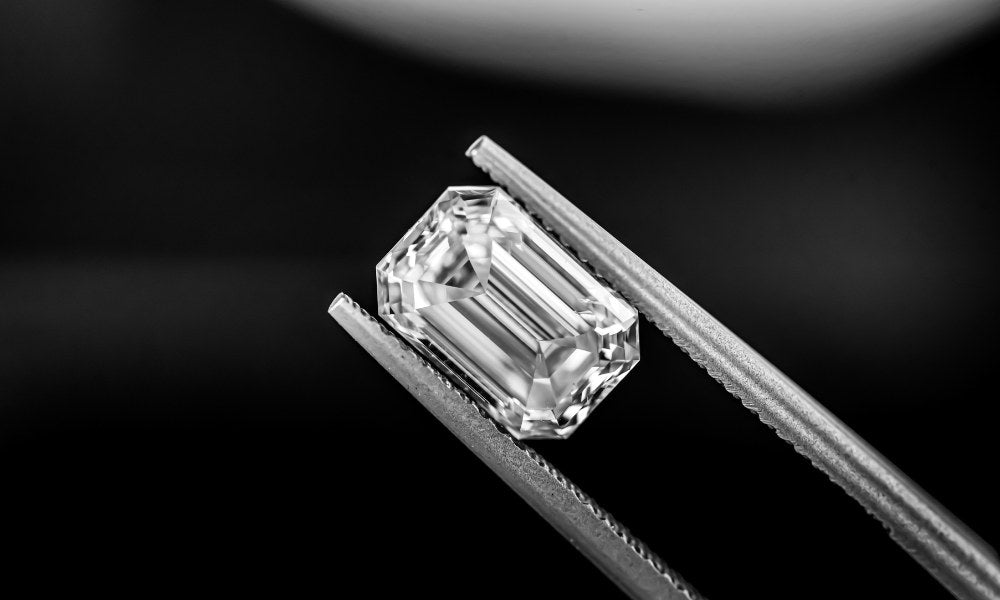 Hochqualitativer Emerald-Cut Labordiamant, gehalten von Präzisionspinzetten, auf schwarzem Hintergrund für einen luxuriösen und nachhaltigen Eindruck. Perfekt für nachhaltigen Schmuck.